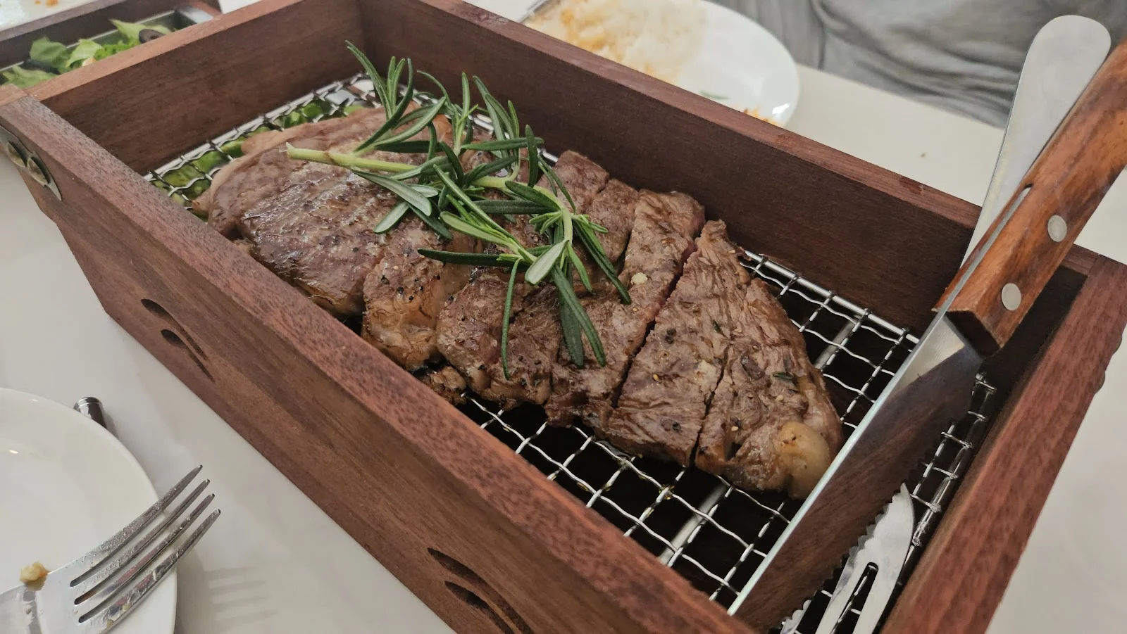우드 그릴 박스 안에 스테이크와 로즈마리가 올려져 있는 사진